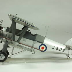 Silver model biplane model with red, white, blue rondels on wings and fuselage. Silver propeller. Profile.