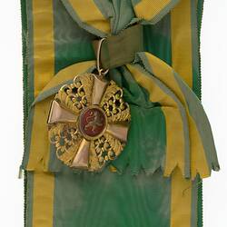 Metal badge attached to green ribbon with yellow edging.