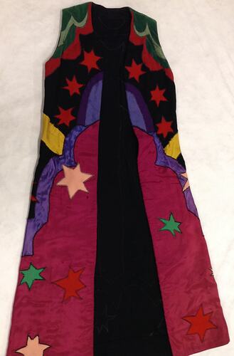 Colourful sleeveless coat with stars and shapes. Mostly black at top and red at bottom.