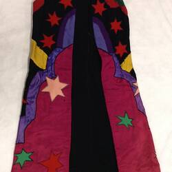 Colourful sleeveless coat with stars and shapes. Mostly black at top and red at bottom.