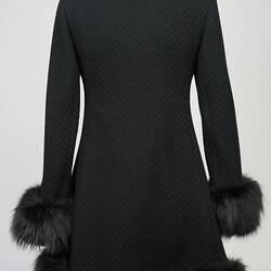 Back of black woollen double-breasted coat with fur collar, cuffs and hem.