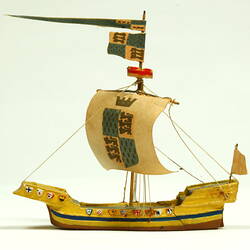 Side view of ship with yellow hull and painted sail.