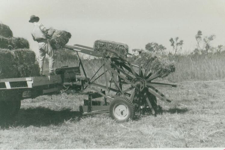 A man lifting a bale of hay from a Sunlifter onto the back of a tray truck.