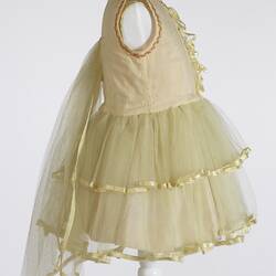 Back of yellow child's dress, sleeveless, layered lace skirt, gold trim. Right profile.