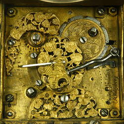 Decorative table clock, square gilded brass case on four feet. Underside view. Engraving detail.