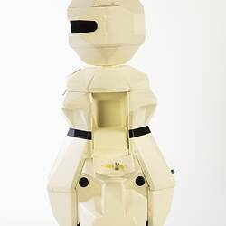 Side view of cream plastic robot with angular human-like shape, ie. head, shoulders, waist and legs. Black plastic features.