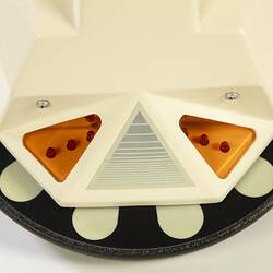 Detail of base of cream plastic robot with angular human-like shape, ie. head, shoulders, waist and legs. Black plastic features.