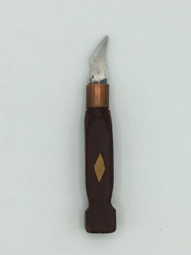Knife with carved dark wooden handle and small blade. Lighter wooden diamond in handle centre.