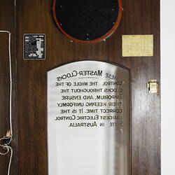 Wooden clock detail of open cabinet glass door with gold lettering.