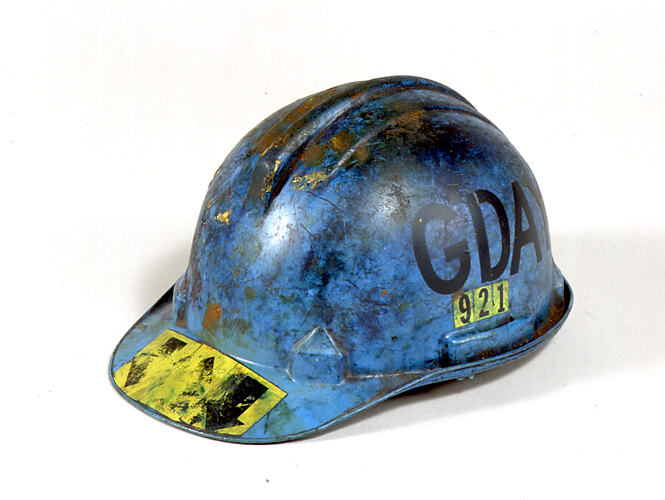 Blue plastic safety helmet with yellow and black stickers on exterior. Marked and scuffed.