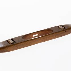 Wooden shuttle with a piece of thick wire through cut out centre. Two wooden rollers underneath shuttle.