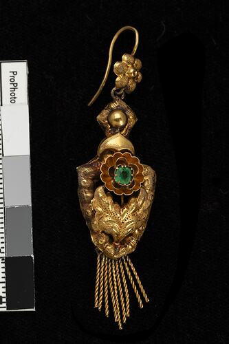 Gold and green paste pendant earring. Comprised of four connected sections with floral and leaf motifs. Gold fringe hangs from the bottom.