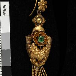 Gold and green paste pendant earring. Comprised of four connected sections with floral and leaf motifs. Gold fringe hangs from the bottom.