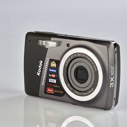 Black and grey camera with metal trim on back, sides and around the lens. Three quarter view.