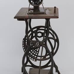 Sewing machine fitted to a metal frame with a wooden bench.