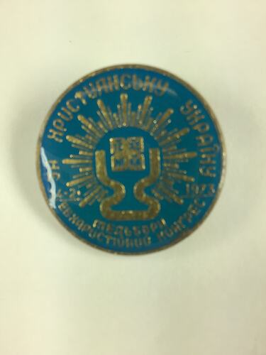 Round light blue badge with gold lettering and pattern.