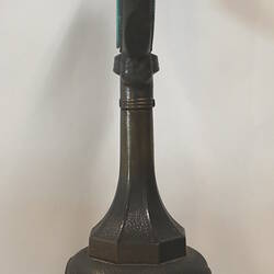 Clock with clear glass face on dark green painted stand, side view.