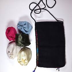 Black fabric sleeve with string. Beside it 5 fabric round jacks in blue, pink, cream, green and white.