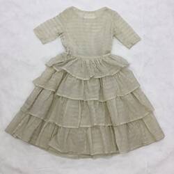 Short sleeve, round neck, cream dress with fine gold horizontal stripes. Four frilled layer skirt.