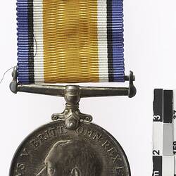 Round medal with profile of man and text surrounding and multicoloured ribbon.
