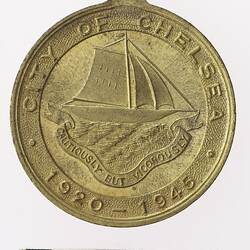 Round gold coloured medal with ship above banner and text surrounding.