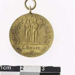 Round gold coloured medal with man and woman surrounded by wreath.