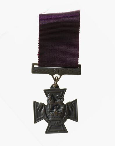 Cross shaped medal with crowned lion standing on royal crown. Semi-circular scroll below. Burgundy ribbon.