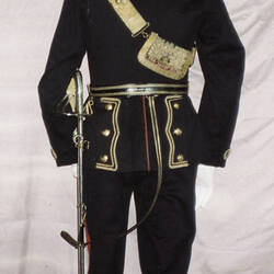 Black military uniform jacket on mannequin, with red collar and gold embroidery waist, back view.