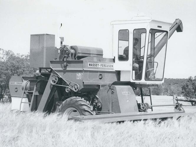 Man driving an auto header harvester in field.