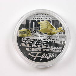 Coin, round, yellow coloured flying biplane. Text behind and below.