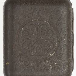 Back of dark metal decorative case with hinges along right edge.
