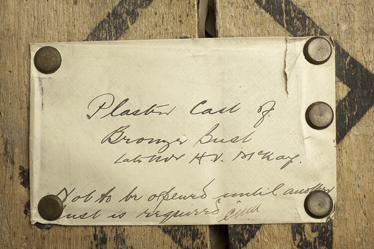 Envelope with handwriting in black ink pinned to wooden box.