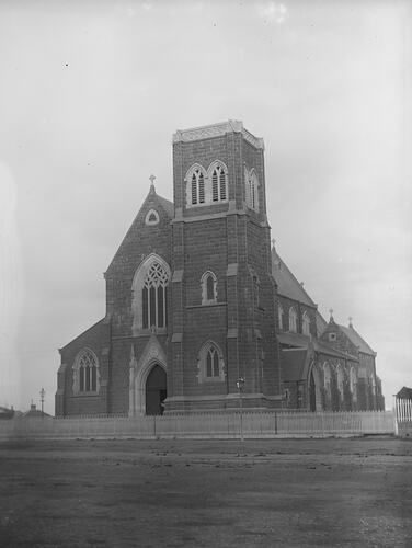 Front view of Roman Catholic church. Entry and belfry tower section. Picket fence and dirt road in front.