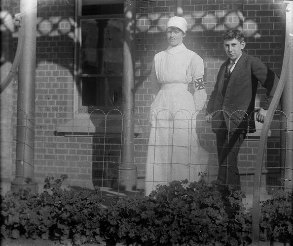 Young woman in nurse's uniform and teenage boy stand on a verandah.