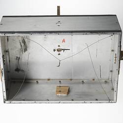 View underneath silver metal and plastic box with a metal rod protruding from top and both sides.