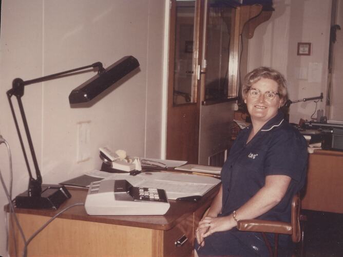 Woman in blue uniform at office desk.