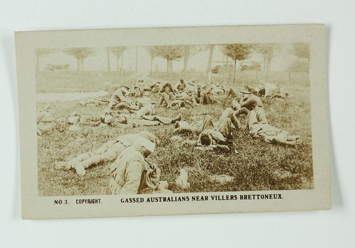 Group of servicemen sitting and laying on grass, trees in background.