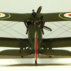 Dark green model airplane. Circle pattern on top on each wing. Back view.