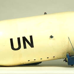 White model airship with blue nose, wings. Black UN on side. Small wheels below. Right profile.