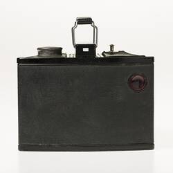 Black cube shaped all metal camera. Carry handle on the top plate. Rear view.