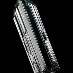Dark green prsimatic crystal on black background.