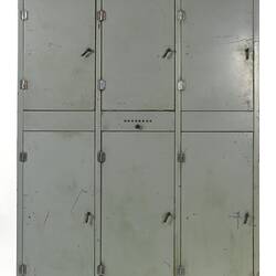 Grey metal cabinet, six closed doors. Central section has small dial.