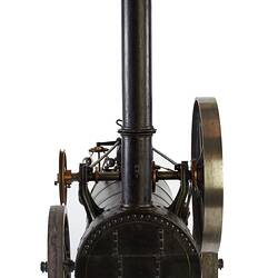 Model of black moveable steam engine on four wheels with tall chimney at front. Front view.