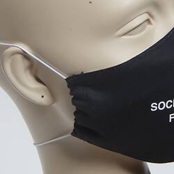 Black face mask with white lettering. Three quarter view showing white band around ear.