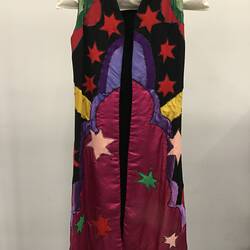 Colourful sleeveless coat with stars and shapes. Mostly reds and black.