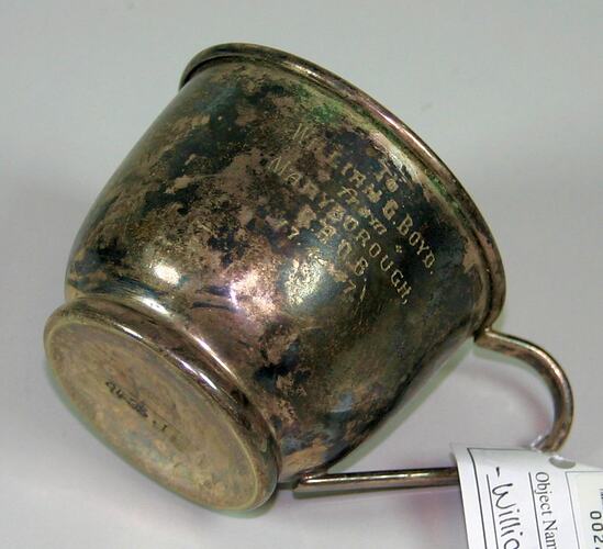 Tarnished metal cup with handle. Engraved text.