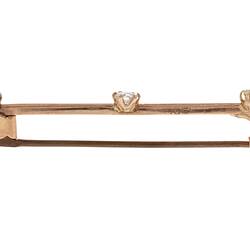 Profile of rose gold bar brooch with three gemstones. Purple amethyst at left end, diamond in centre and light green peridot at right end.