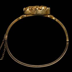 Profile of gold bangle (bracelet) featuring a large gold nugget. Fine chain at left.