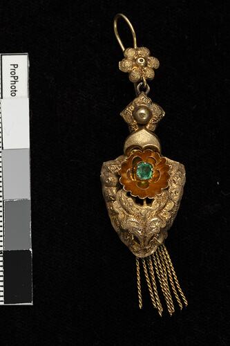Gold and green paste pendant earring. Comprised of four connected sections with floral and leaf motifs. Gold fringe hangs from the bottom.