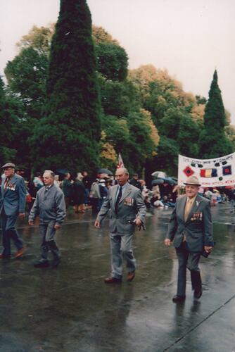 Men wearing suits and medals marching in a parade.